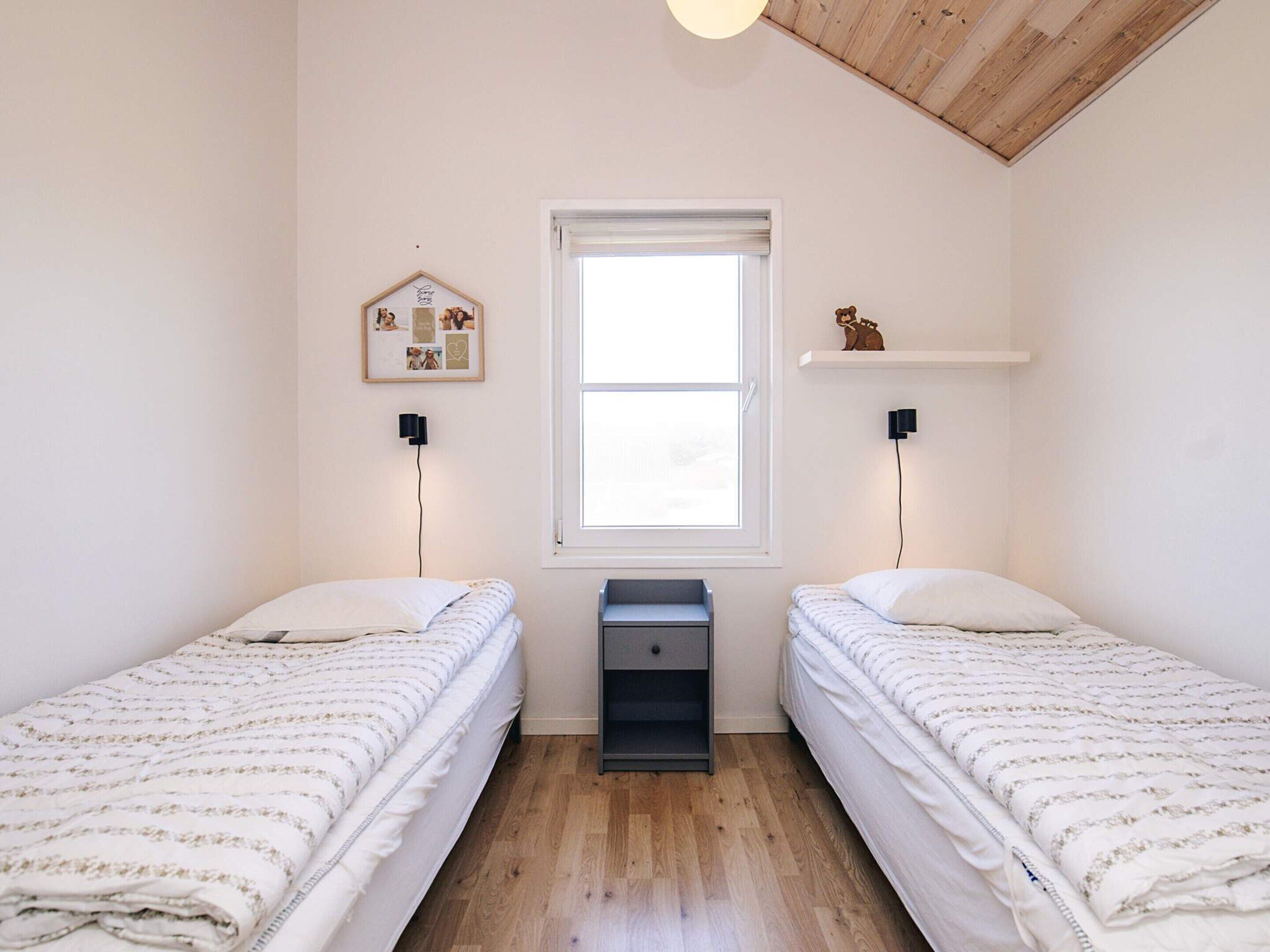 A room with two beds, a window, a small table, and a wall-mounted shelf.