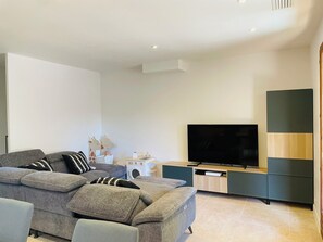 Ein modernes Wohnzimmer mit einem grauen Modulsessel, einem Flachbildfernseher und einer Holz-Unterhaltungsecke.