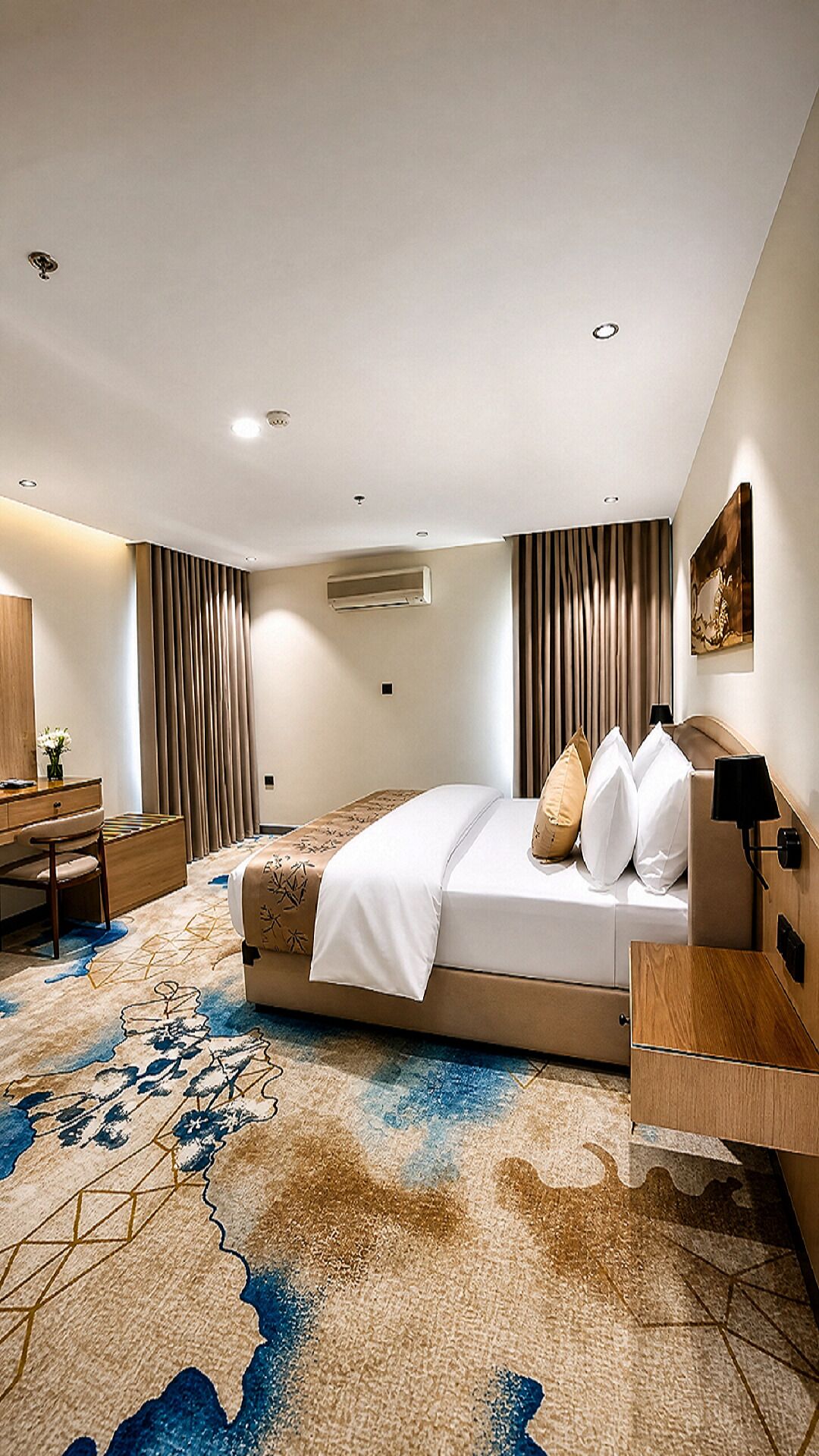 A hotel room with a bed, a desk, a chair, a lamp, and a painting on the wall.