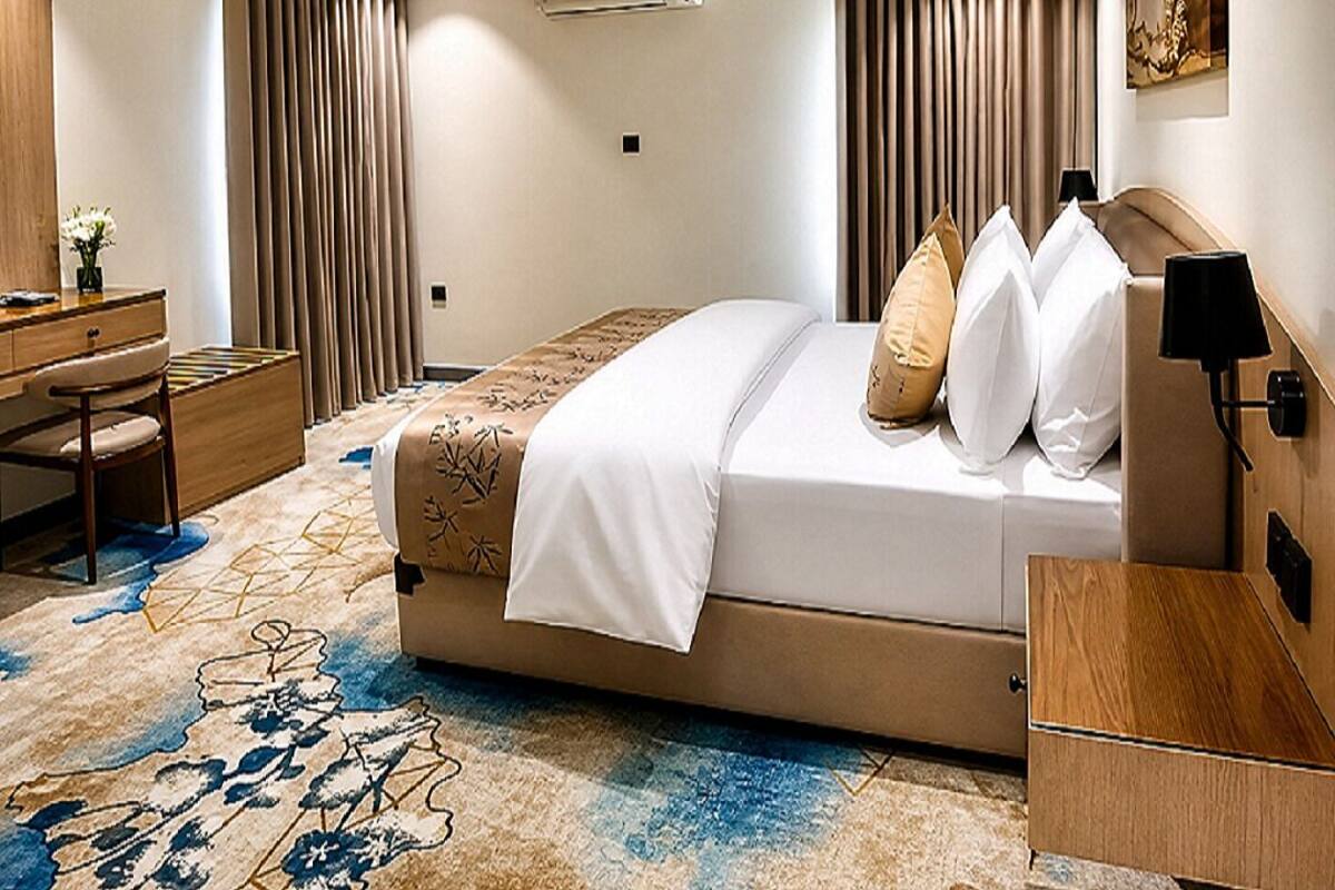 A hotel room with a bed, a desk, a chair, a lamp, and a painting on the wall.