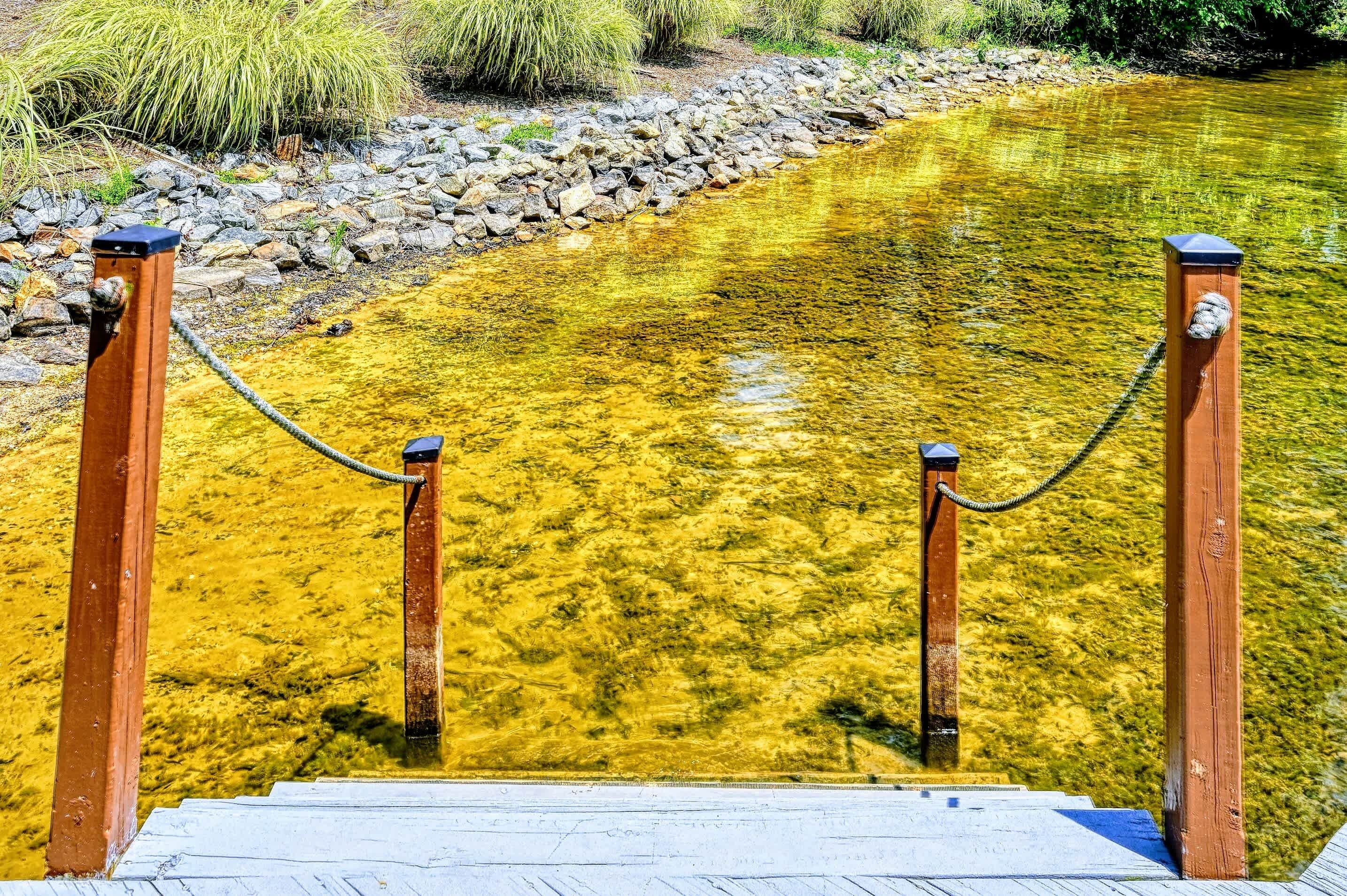 A wooden dock with a chain barrier leading into a clear yellowish river.