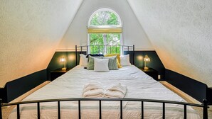 Un dormitorio con una cama, dos lámparas de noche, un ventanal y vista a árboles.