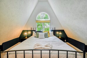 Un dormitorio con una cama, dos lámparas de noche, un ventanal y vista a árboles.