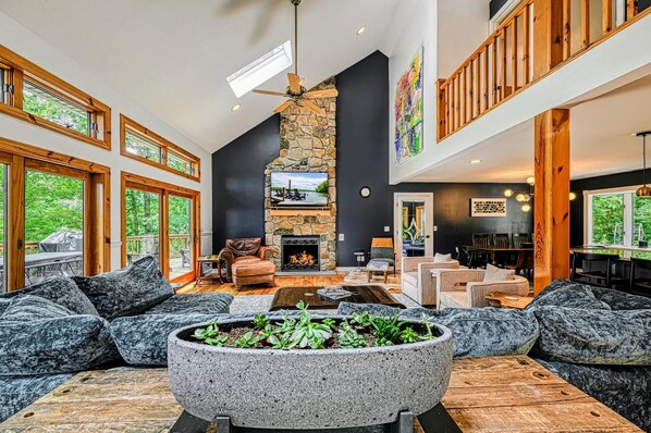 Un salón espacioso con chimenea de piedra, ventanas amplias y un techo alto.