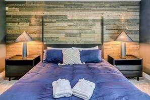 Una camera da letto con una testiera in legno, due comodini con lampade, un letto con copriletto blu e una coppia di asciugamani sul letto.