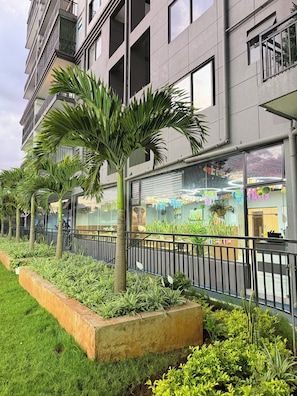 A modern building with balconies, a glass storefront, and a landscaped garden with palm trees. - Studio in kileleshwa (Nairobi)