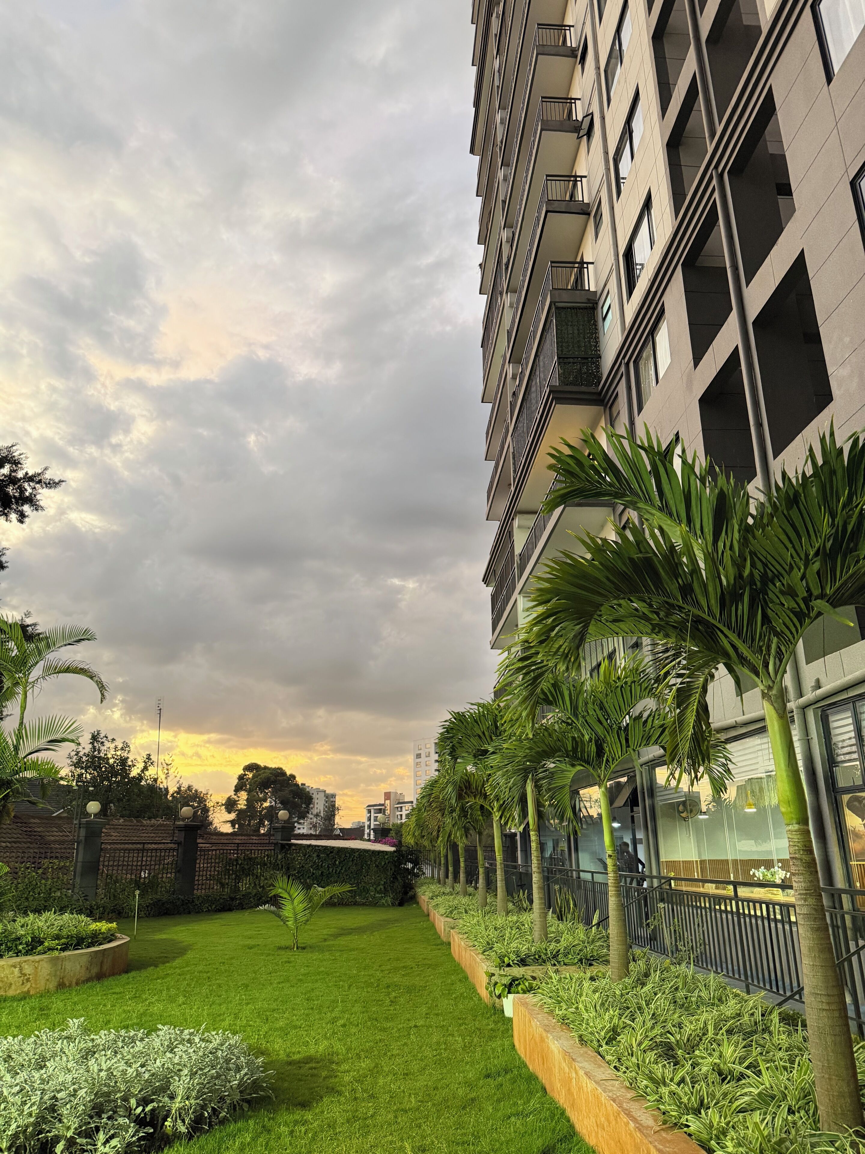 Un edificio moderno con balconi, un giardino curato con prato e piante, e un cielo nuvoloso.