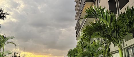Un edificio moderno con balcones, un jardín cuidado con césped y plantas, y un cielo nublado.