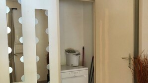 A room with a white washing machine, a door with a mirror, and a vase with tall grasses.