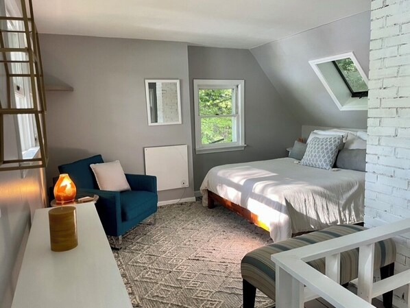 Une chambre Ă coucher avec un lit, un canapĂ© bleu, une table basse blanche, une lampe, une fenĂȘtre et un plafond en pente.