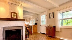 Una habitación con chimenea, piso de madera, una escalera y un ventanal con vista a árboles.