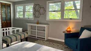 Un dormitorio con cama, sofá azul, mesa consola blanca y ventana con vista a árboles.
