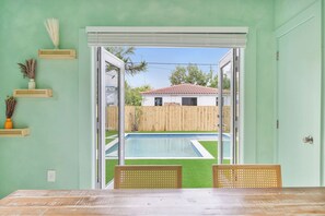 A room with a sliding glass door leading to a backyard with a pool and a wooden fence. - Design District House (Miami)