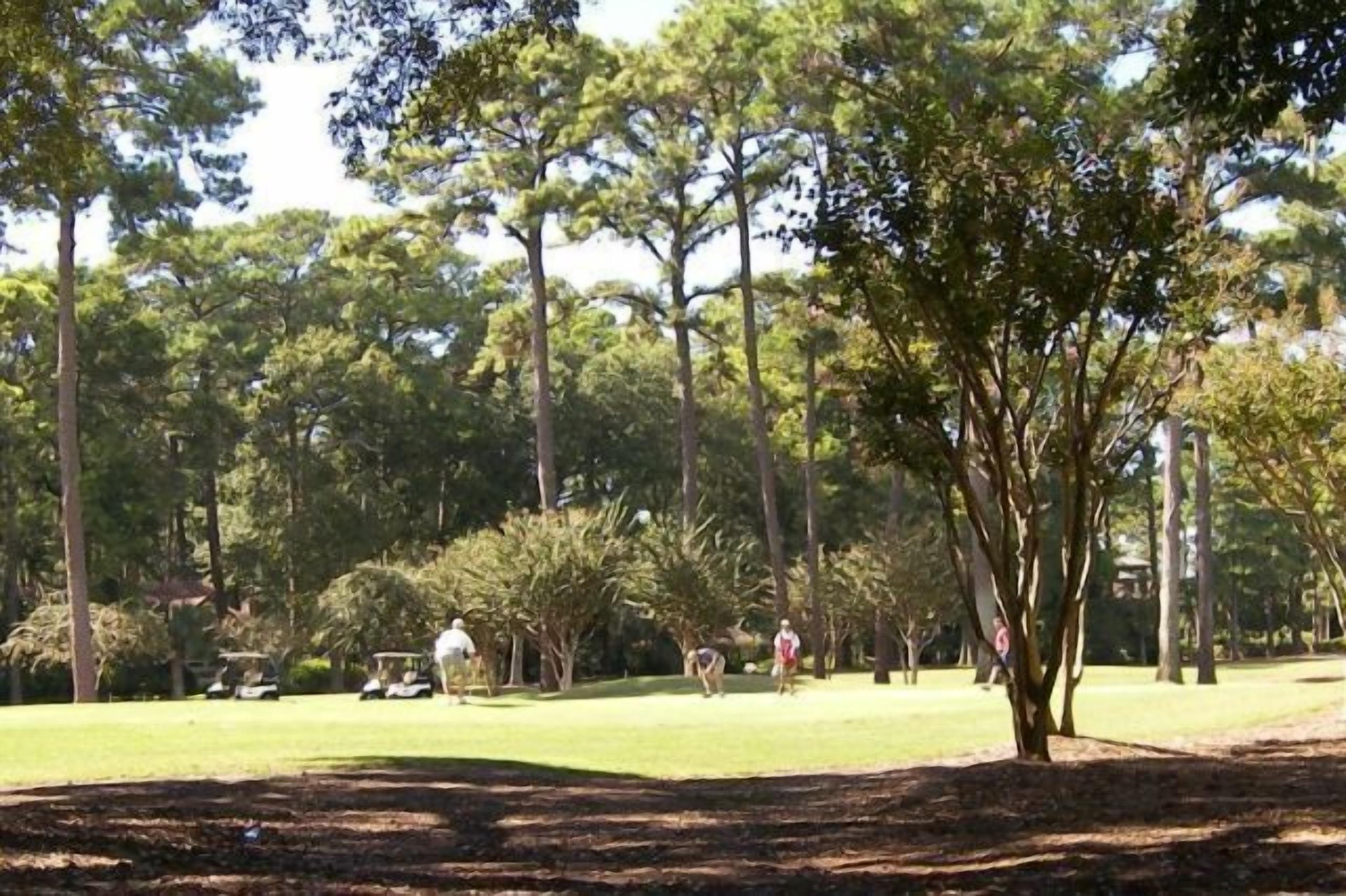 A golf course with trees, a golf cart, and people playing.