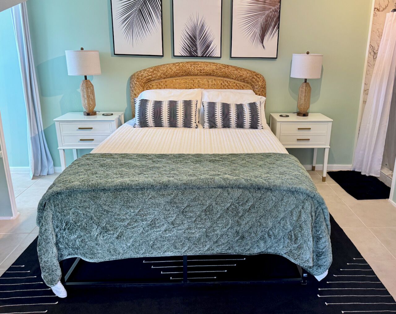 A bed with a textured blanket, two bedside tables with lamps, and three framed leaf artworks on the wall.