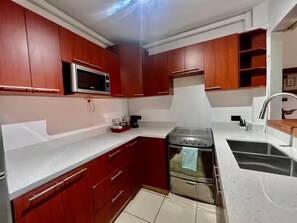 A kitchen with red cabinets, a microwave, a stove, and a sink. - Renovated Apartment: 3 Bedrooms, with AC in the Living Room and a Pool (San Salvador)
