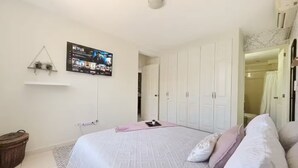 Een slaapkamer met een bed, een aan de muur bevestigde televisie, een garderobe en een klein plankje met planten.