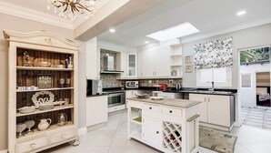 A modern kitchen with white cabinetry, a central island, a decorative wooden shelf, and a chandelier. - Luxurious & Spacious Home in the heart of Sandton (Sandton)