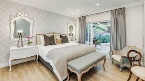 A bedroom with a large bed, a nightstand, a dresser, a bench, and a chair. - Luxurious & Spacious Home in the heart of Sandton (Sandton)