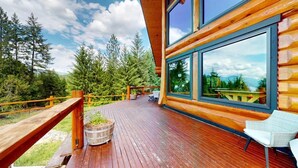 A wooden deck with a view of a forest, a large window, and a chair.