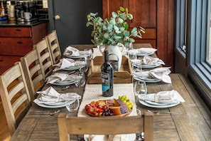 A wooden dining table set with plates, glasses, and a bottle of wine. - Family retreat + NEW HOT TUB, Game Room, Views | Near RMNP+ Grand Lake (Grand Lake)