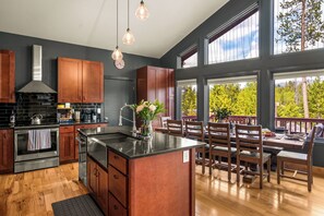 A modern kitchen with wooden cabinets, a large island, and a dining area with a view of trees. - Game Room, Fire Pit & Views |Near RMNP+Grand Lake (Grand Lake)