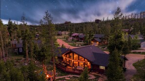 Un chalet doté d’une terrasse, entouré d’arbres, sous un ciel étoilé.