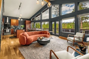 A modern kitchen with wooden cabinets, a dining area with a round table, and a large window overlooking a forest. - Game Room, Fire Pit & Views |Near RMNP+Grand Lake (Grand Lake)