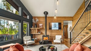 Un salon moderne avec une cheminée, des murs en bois et une grande fenêtre donnant sur les arbres.