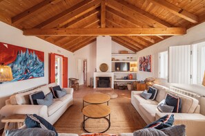 Een ruime woonkamer met hoog houten plafond, een open haard en een groot schilderij aan de wand.