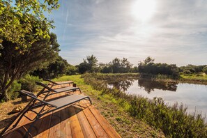Eine Holzterrasse mit Liegestühlen an einem stillen Gewässer, umgeben von viel Grün.