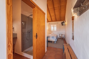 A wooden door leading to a shower area with a tiled wall, a bed with a white headboard, and a small table with chairs.
