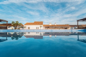 Una piscina amb el reflex clar d'un edifici de façana blanca i teulat llisot.