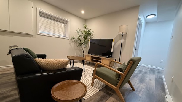 Een moderne woonkamer met een bank, fauteuil, ronde houten tafel, tv-meubel en een potplant.
