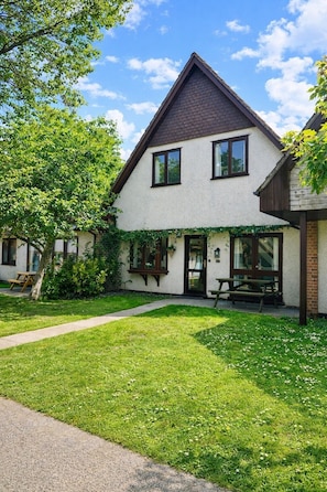 A two-story house with a sloped roof, a front porch, and a well-maintained lawn.