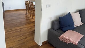 Un salon moderne avec un canapé gris, une table à manger en bois et des chaises, et un couloir menant à une autre pièce.
