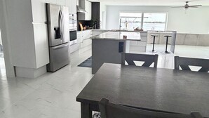 Eine moderne Küche mit integriertem Kühlschrank, einem Essbereich mit Tisch und Stühlen sowie Blick ins Freie durch ein großes Fenster.
