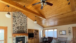 A spacious living room with a stone fireplace, wooden ceiling, and a large sofa.