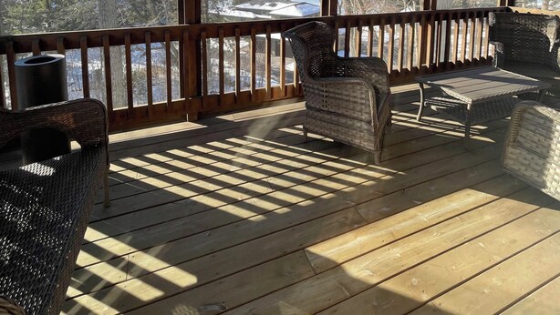 A covered outdoor deck with a ceiling fan, wicker furniture, and a view of a snowy landscape.
