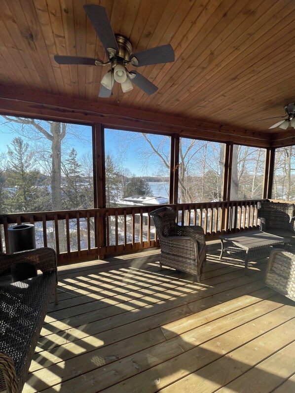 A covered outdoor deck with a ceiling fan, wicker furniture, and a view of a snowy landscape.