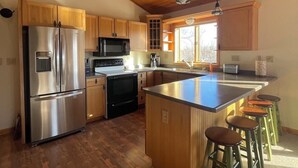 A modern kitchen with wooden cabinets, stainless steel appliances, a central island with stools, and pendant lighting.