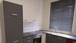 Una cocina con gabinetes grises, un lavamanos y un ventanal con persianas.