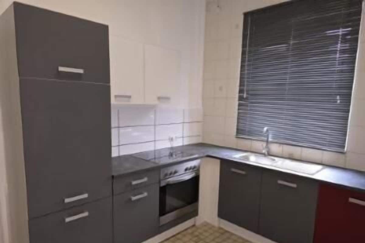 A kitchen with grey cabinets, a sink, and a window with blinds.