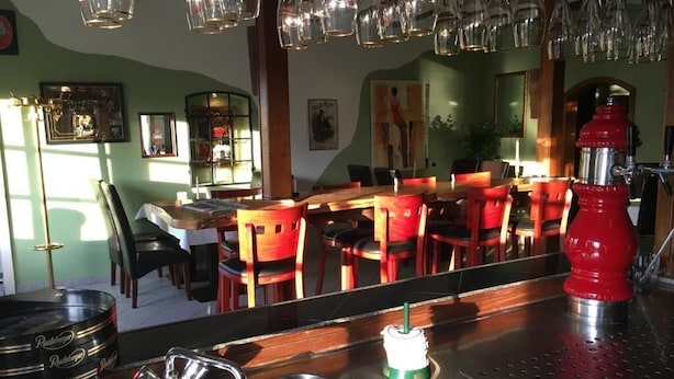 Interior de restaurante con barra, sillas rojas, una máquina de café roja y lámparas colgantes.