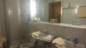 Un baño con dos lavamanos, un inodoro, una ducha y un espejo.
