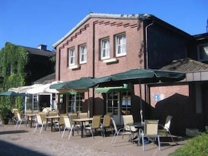 A building with outdoor seating and umbrellas, a brick facade, and a clear sky. - Hotel Zur Buche (Bark)