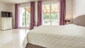A bedroom with a large bed, a television on a dresser, and a view of trees through the window. - Pool & Garden Villa Lelia (Veneto)