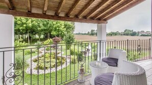 A covered balcony with a view of a garden and pond, white wicker furniture, and a metal railing. - Pool & Garden Villa Lelia (Veneto)