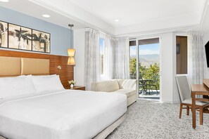 A hotel room with a large bed, a sofa, a desk, and a balcony with a view of the mountains. - Resort in marvelous Palm Desert on the Coachella shuttle bus route. 1 bedroom (Palm Desert)