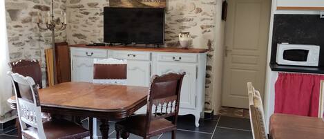 A dining area with a stone wall, a television, a microwave, and a dining table with chairs.